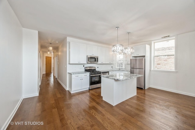 kitchen featuring pendant lighting, stainless steel appliances, white cabinetry, a kitchen island, and a sink