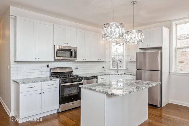 kitchen with light stone counters, stainless steel appliances, a sink, a kitchen island, and white cabinets