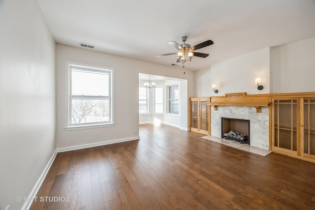 unfurnished living room with visible vents, a premium fireplace, wood finished floors, baseboards, and ceiling fan with notable chandelier