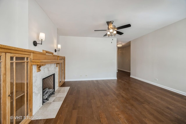 unfurnished living room with a ceiling fan, a premium fireplace, baseboards, and wood finished floors