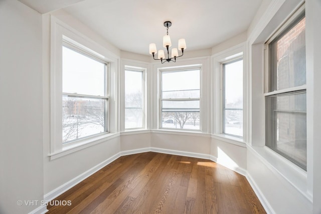 unfurnished dining area featuring an inviting chandelier, baseboards, dark wood-style flooring, and a wealth of natural light