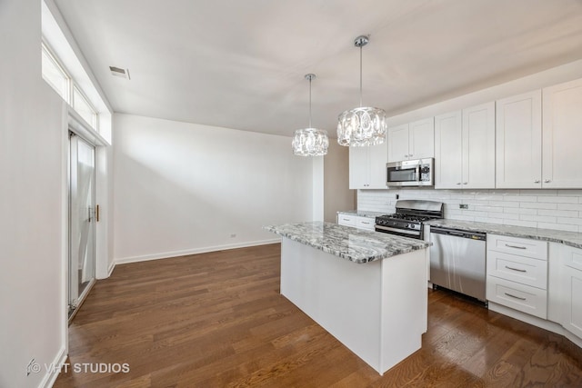 kitchen with light stone counters, appliances with stainless steel finishes, white cabinetry, and a center island