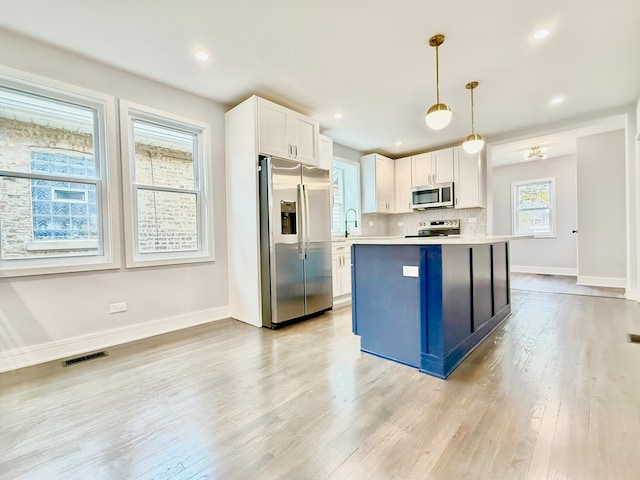 kitchen with white cabinets, decorative light fixtures, stainless steel appliances, and light hardwood / wood-style floors