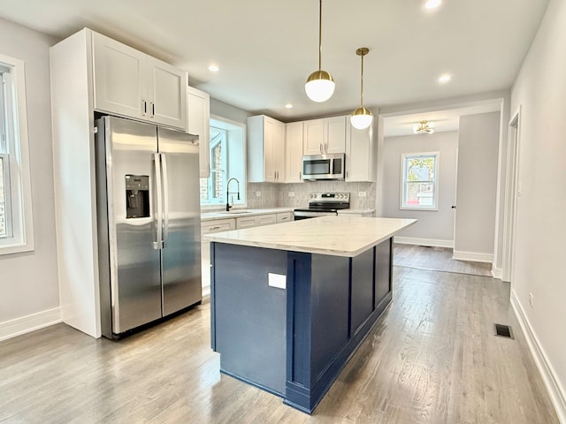 kitchen with decorative light fixtures, stainless steel appliances, white cabinetry, and a kitchen island