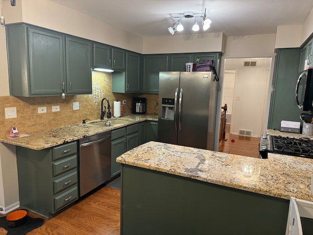 kitchen with light hardwood / wood-style floors, sink, kitchen peninsula, light stone counters, and appliances with stainless steel finishes