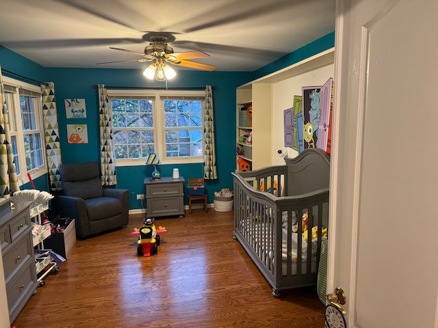 bedroom with dark wood-type flooring, ceiling fan, and a nursery area