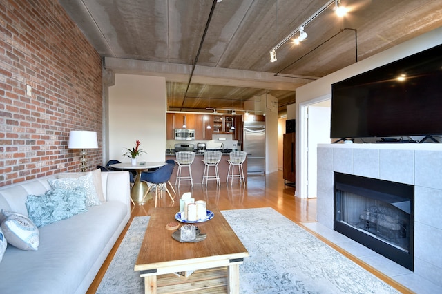 living room featuring a fireplace, rail lighting, brick wall, and light wood-type flooring