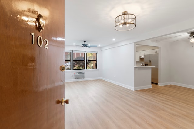 unfurnished living room featuring a wall unit AC, ceiling fan with notable chandelier, and light hardwood / wood-style flooring