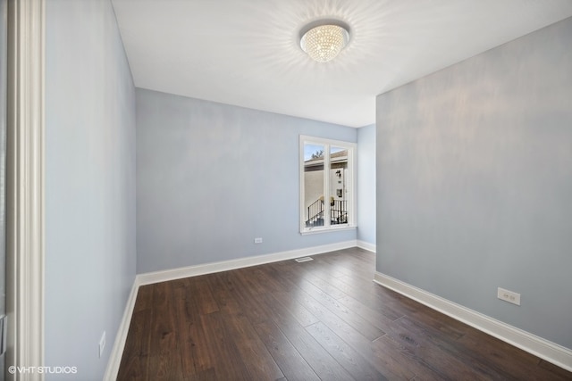 empty room with dark hardwood / wood-style flooring and a chandelier