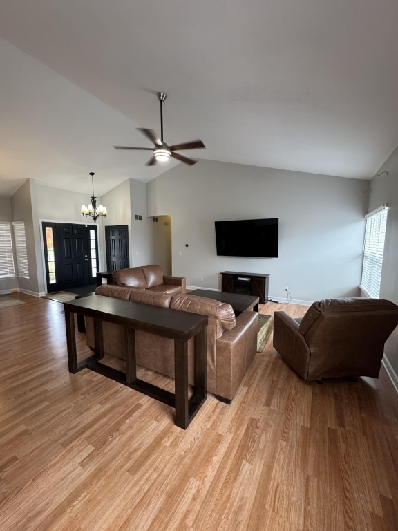 living room with light hardwood / wood-style floors, ceiling fan with notable chandelier, and vaulted ceiling