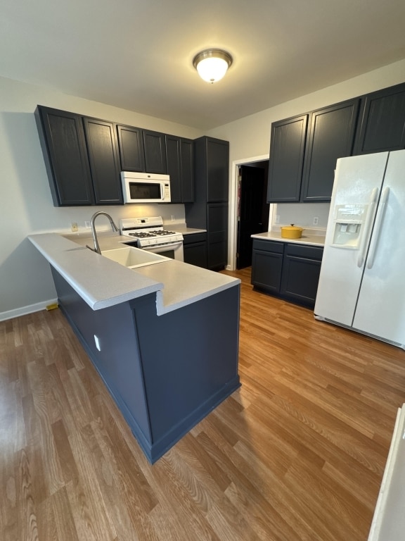 kitchen featuring white appliances, sink, light hardwood / wood-style flooring, and kitchen peninsula