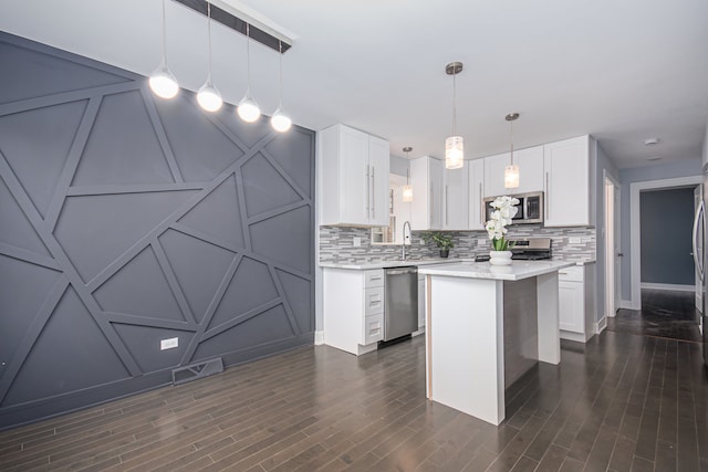 kitchen featuring stainless steel appliances, hanging light fixtures, a kitchen island, backsplash, and white cabinetry