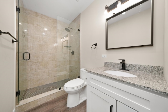 bathroom featuring toilet, vanity, wood-type flooring, and a shower with door