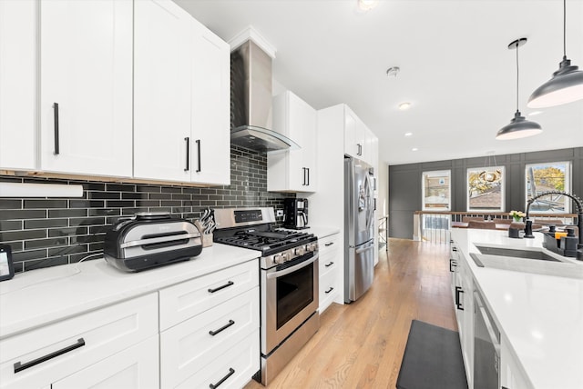 kitchen with wall chimney range hood, appliances with stainless steel finishes, hanging light fixtures, sink, and white cabinets