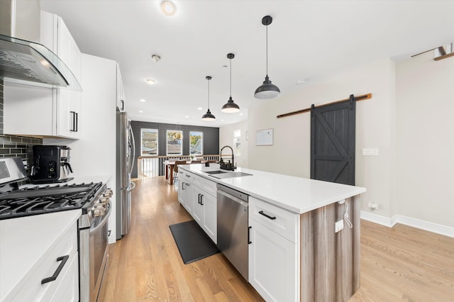 kitchen featuring stainless steel appliances, a barn door, sink, a kitchen island with sink, and wall chimney range hood