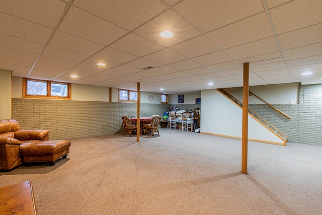 basement with carpet flooring, a paneled ceiling, and brick wall