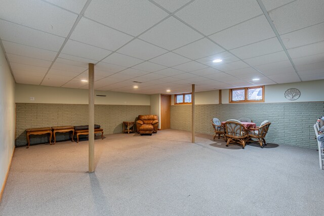 recreation room with carpet flooring, a drop ceiling, and brick wall