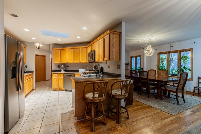 kitchen with kitchen peninsula, a skylight, stainless steel appliances, sink, and light hardwood / wood-style floors