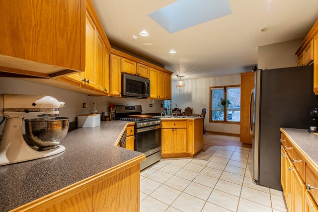 kitchen with a skylight, sink, kitchen peninsula, light tile patterned floors, and appliances with stainless steel finishes