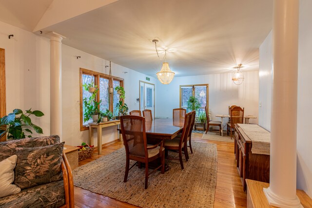 dining area with decorative columns, light hardwood / wood-style floors, and a notable chandelier