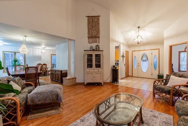 living room featuring light wood-type flooring, an inviting chandelier, ornate columns, and plenty of natural light