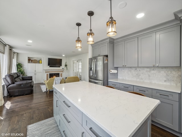 kitchen with gray cabinets, dark hardwood / wood-style floors, light stone countertops, pendant lighting, and stainless steel fridge