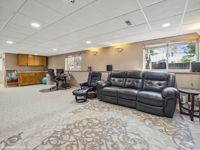 living room with built in desk, a drop ceiling, and light colored carpet