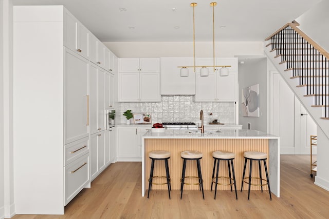 kitchen with a kitchen bar, sink, white cabinetry, hanging light fixtures, and an island with sink