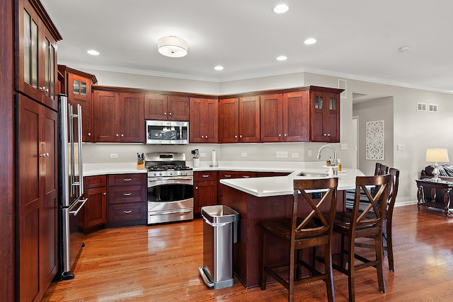 kitchen with stainless steel appliances, sink, kitchen peninsula, crown molding, and light wood-type flooring