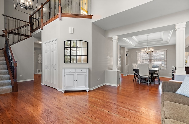 living room featuring wood-type flooring, a raised ceiling, decorative columns, and an inviting chandelier