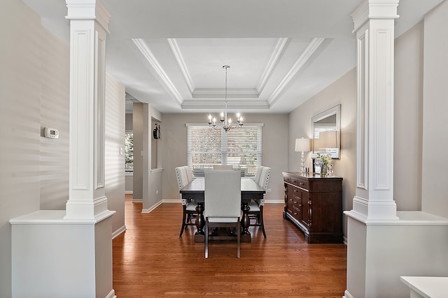 dining area with dark wood-type flooring, decorative columns, a tray ceiling, and a notable chandelier