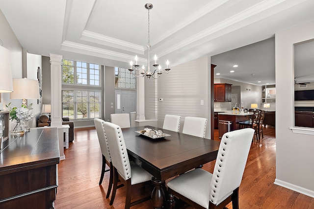 dining area with ornamental molding, dark hardwood / wood-style floors, a chandelier, a raised ceiling, and decorative columns