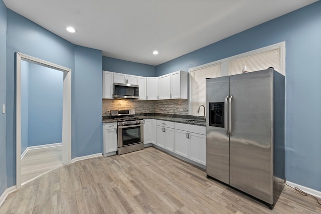 kitchen with white cabinetry, decorative backsplash, appliances with stainless steel finishes, and light hardwood / wood-style flooring