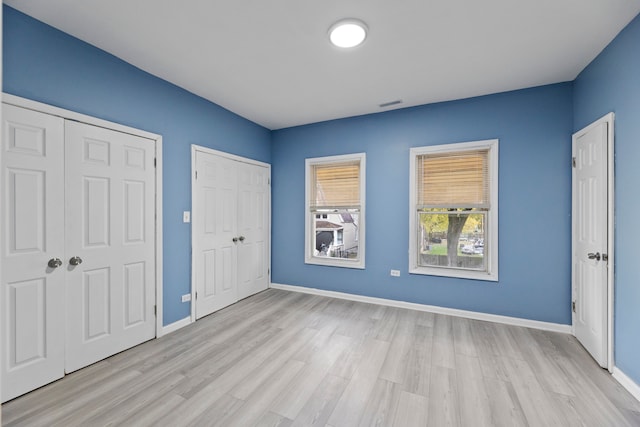 unfurnished bedroom featuring light wood-type flooring and two closets