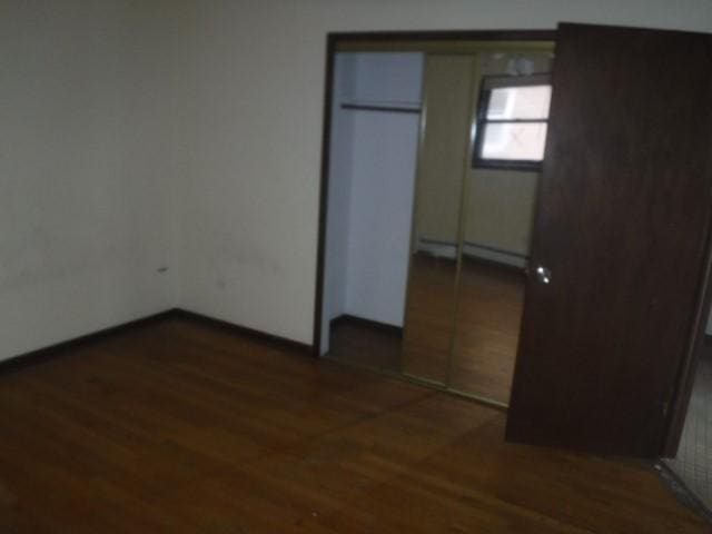 unfurnished bedroom with dark hardwood / wood-style floors, a closet, and a baseboard heating unit