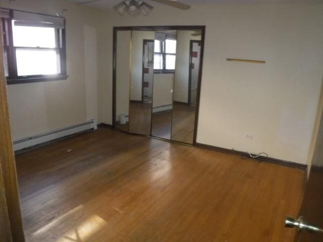 unfurnished bedroom with ceiling fan, a closet, wood-type flooring, and a baseboard heating unit