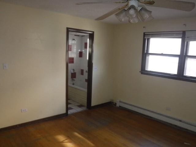 unfurnished bedroom featuring baseboard heating, ceiling fan, ensuite bathroom, and dark wood-type flooring