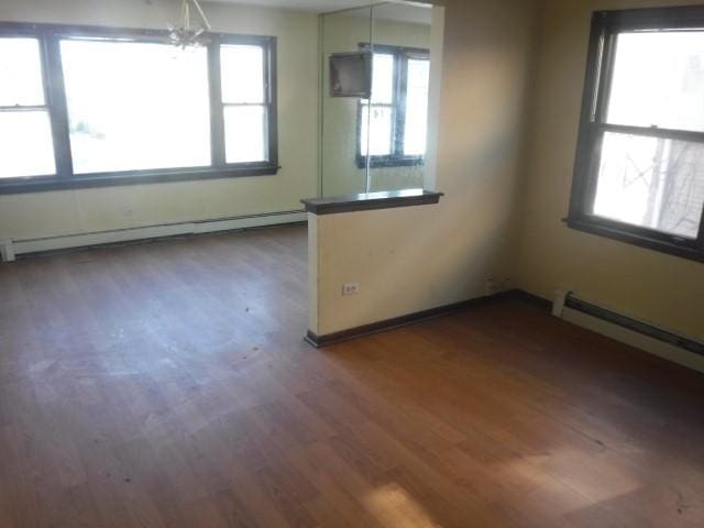 unfurnished room featuring dark hardwood / wood-style flooring, a baseboard radiator, and an inviting chandelier