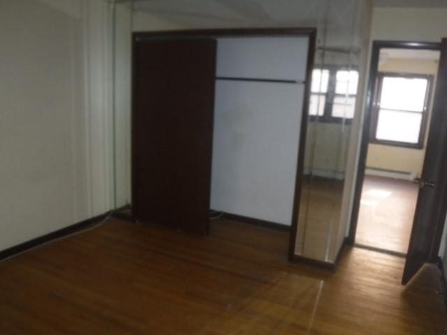 unfurnished bedroom featuring dark hardwood / wood-style flooring and a baseboard radiator