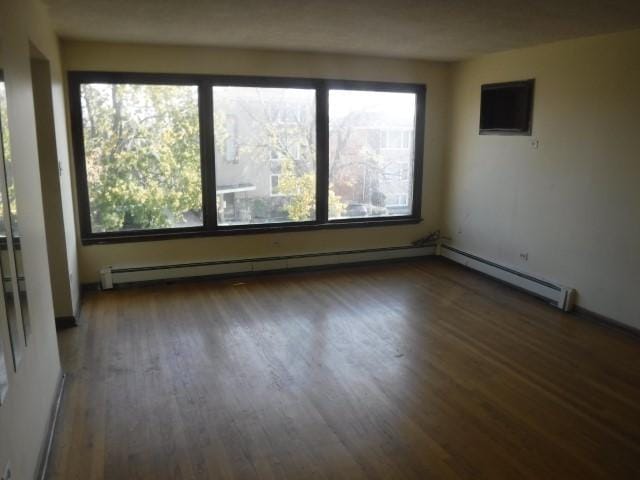 empty room with dark hardwood / wood-style flooring and a baseboard radiator