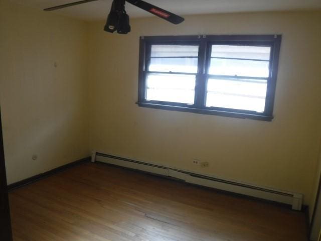 spare room with wood-type flooring, ceiling fan, and a baseboard heating unit