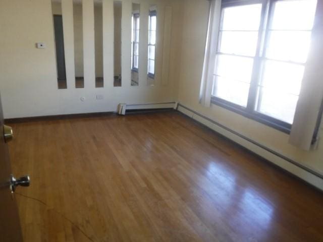 empty room featuring dark wood-type flooring, a healthy amount of sunlight, and a baseboard radiator