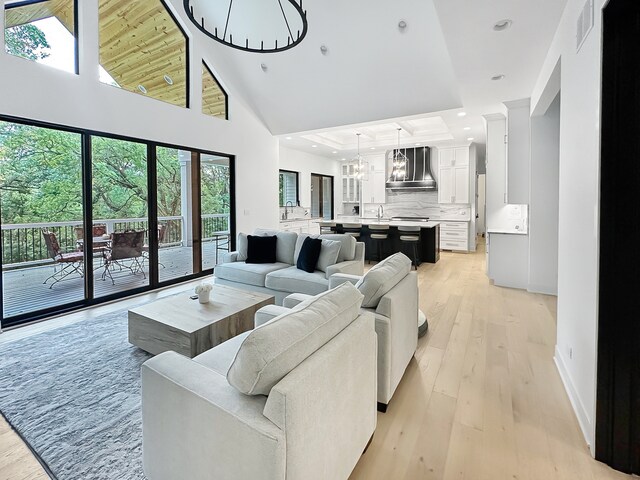 living room featuring a healthy amount of sunlight, light hardwood / wood-style flooring, high vaulted ceiling, and a notable chandelier