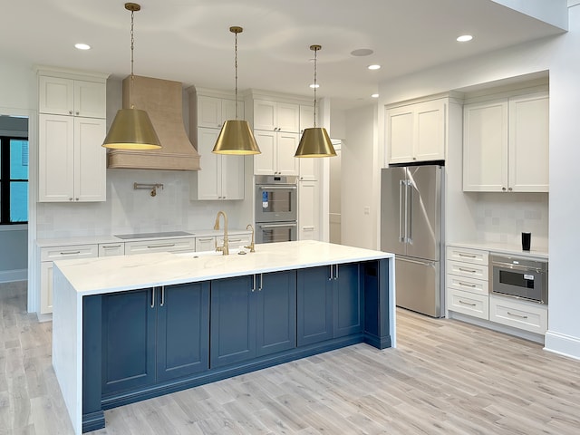 kitchen featuring custom range hood, stainless steel appliances, hanging light fixtures, and an island with sink