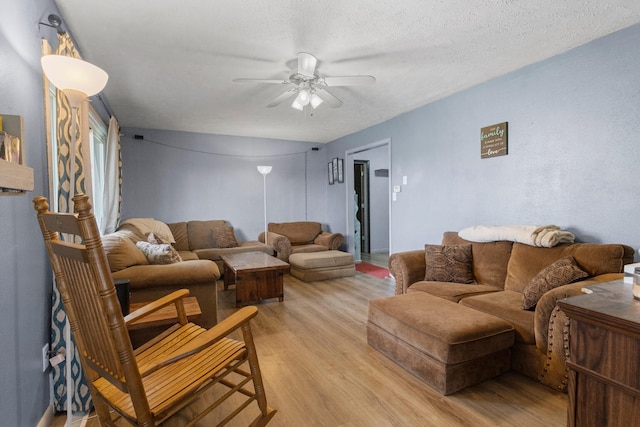 living room with ceiling fan, light wood-type flooring, and a textured ceiling