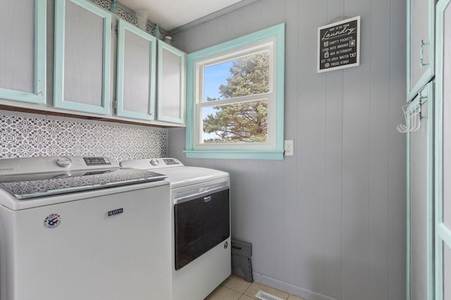 clothes washing area featuring wood walls, washer and clothes dryer, light tile patterned floors, and cabinets