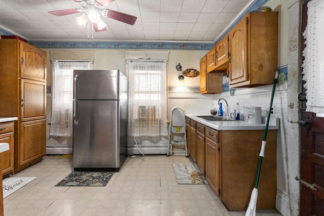 kitchen featuring baseboard heating, stainless steel refrigerator, ceiling fan, and sink