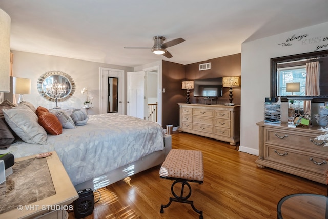 bedroom with ceiling fan with notable chandelier and light hardwood / wood-style flooring