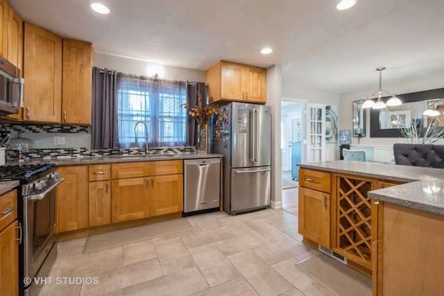 kitchen featuring stainless steel appliances, light stone counters, hanging light fixtures, sink, and tasteful backsplash