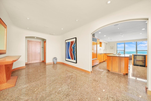 kitchen featuring a kitchen island with sink, a water view, kitchen peninsula, light brown cabinetry, and beverage cooler